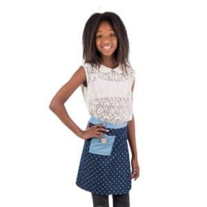 Kleine meisje met lange haar, wit lace top en blauwe rok met hartjes, lachend, staand op witte achtergrond.