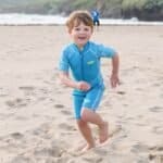 Un enfant enthousiaste joue sur la plage en short de bain, profitant des plaisirs de la mer.