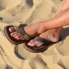 Man draagt Cool Shoe Corp 2LUX Chestnut teenslippers op zandstrand