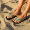 Sandalen met blauwe banden en flips op zandstrand.