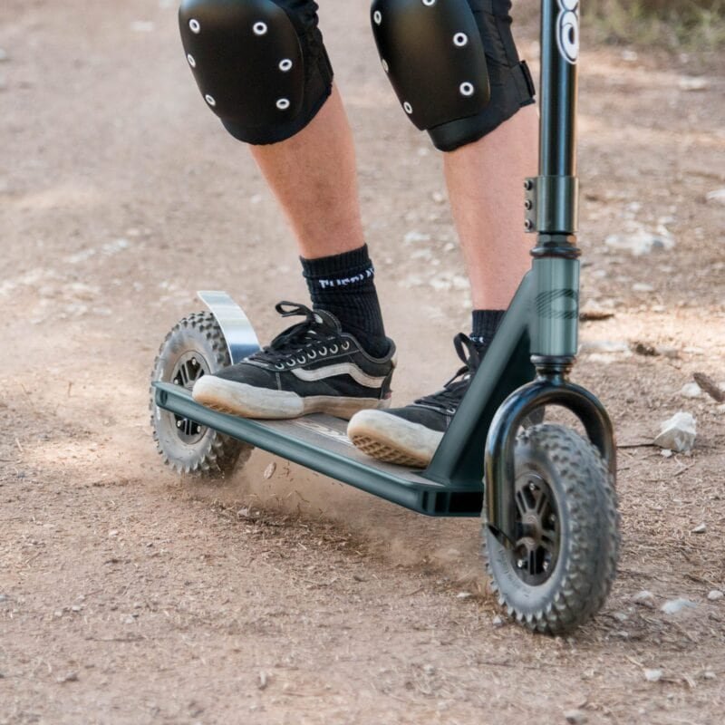 Scooter with pneumatic tyres and protective covers on a dirt road.