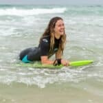 Planche de surf colorée et surfeur souriant dans la mer.
