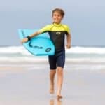 Enfant avec planche de surf sur la plage.