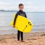 Planche de surf avec enfant sur la plage, sports nautiques, surf, mer, extérieur, été, équipement de sports nautiques, enfant en combinaison.