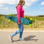 Planche à roulettes colorée avec des roues vertes portée par une femme dans un cadre extérieur décontracté.