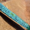 Skateboard joyeux avec impression bleue et détails verts sur la base sable.