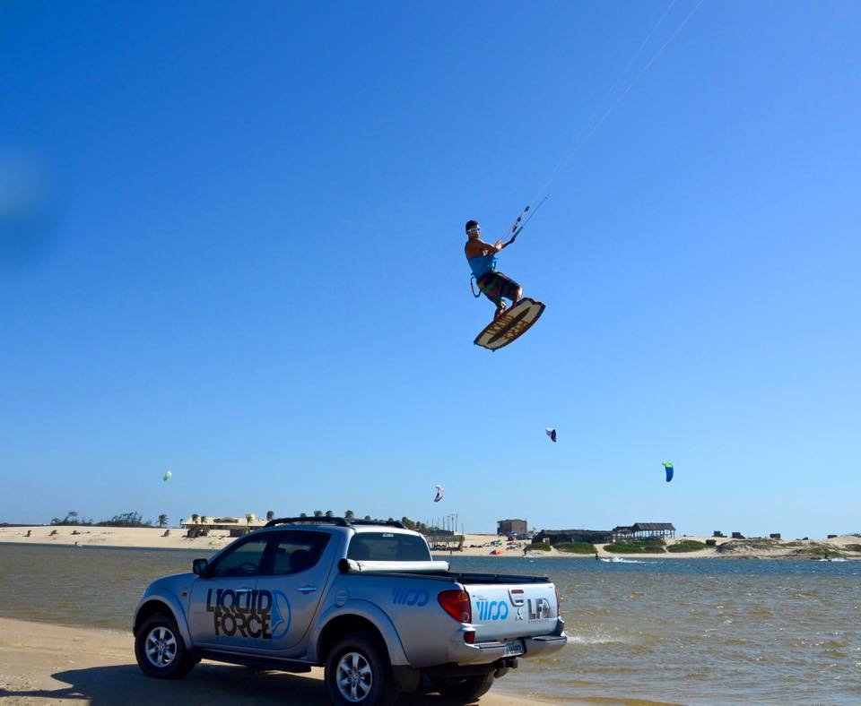 Kitesurfer met Glogglz zonnebril maakt een sprong over een auto aan het strand.