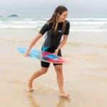 Buntes Surfbrett und Frau am Strand während einer Surfsession.