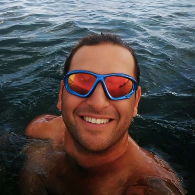 Colourful swimming goggles on a smiling man in the water, enjoying outdoor fun.