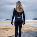 Wetsuit voor surfen of watersporten aan zee, vrouw op strand met branding op achtergrond.