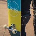 Kleurrijke skateboard met witte wielen en een grip tape logo op het ondervlak.