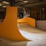 Skater terrein binnen skatepark met houten muren en oranje ramps voor tricks en stunts.