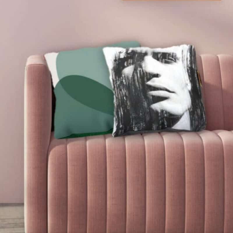 Kissen mit abstraktem schwarz-weißem Frauenporträt und grünem Grafikdesign auf rosa Sofa.