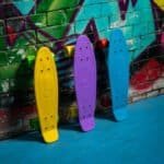 Skateboards in yellow, lilac and blue colours hang from a graffiti wall.