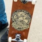 Deel van een houten skateboard met een gedetailleerd grafisch ontwerp van een adelaar en een skateboard met tekst.