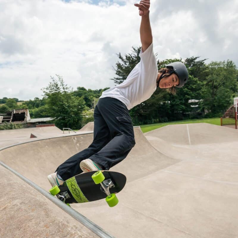 Scheidsrechter in skates en helm op een skatebaan met groene omgeving.