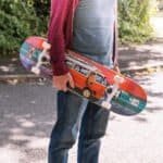 Planche à roulettes colorée avec un dessin de bus, tenue par une personne en tenue décontractée à l'extérieur.