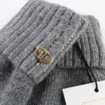 Knitted grey sweater with metallic logo patch and decorative studs.