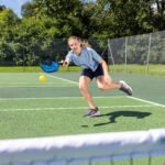 U13 tennis meisje in actie op een groene buiten tennisbaan, spelend met gele tennisbal en racket, sportieve ontspanning.