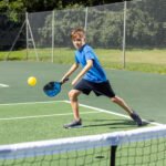 Kind speelt tennis op buitenbaan met racket en zachte bal.