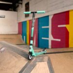 Colourful kick scooter on indoor skating track with graffiti wall in background.