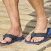 Sandalen met blauwe zool en verstelbare band op houten vlonder.