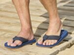Sandalen met blauwe zool en verstelbare band op houten vlonder.